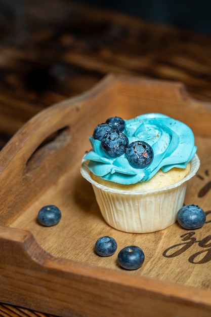 Single sweet homemade cupcake decorated with blue cream cheese topping and blueberries on tray
