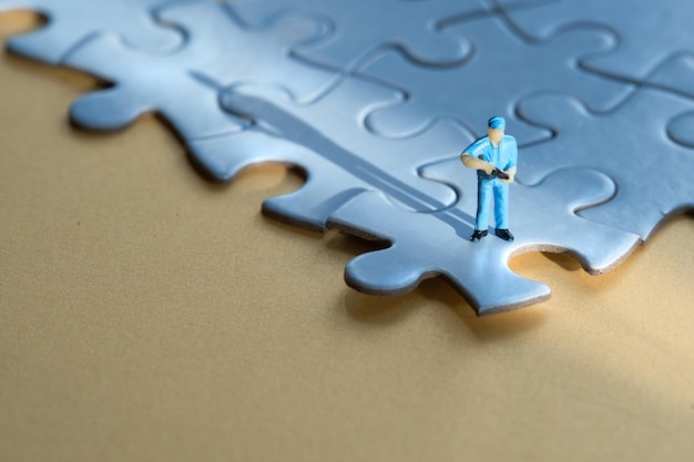 Single tiny worker miniature figure on edge of linked blue jigsaw puzzle Yellow paper background long shadow Concept background with copyspace place for text