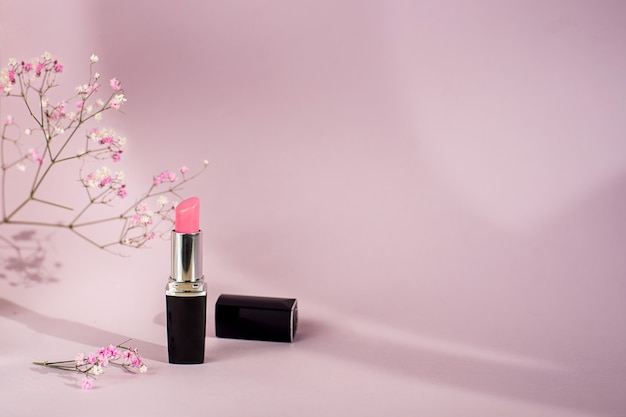 Single tube of pink lipstick on pink background with flowers