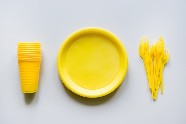 Photo single use picnic yellow utensils, plates, cups, forks on grey.