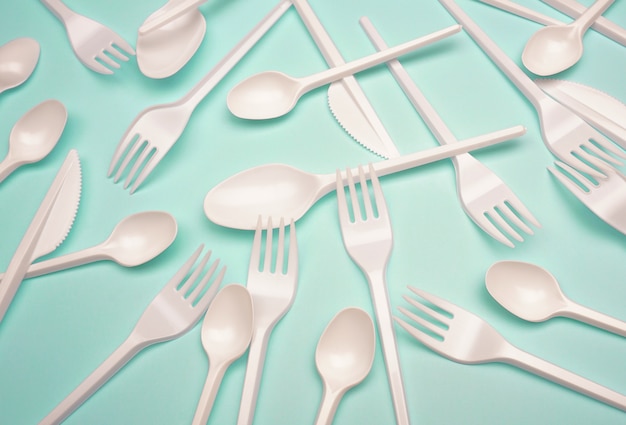 Single-use plastic products: plastic cutlery, cups on bright blue background