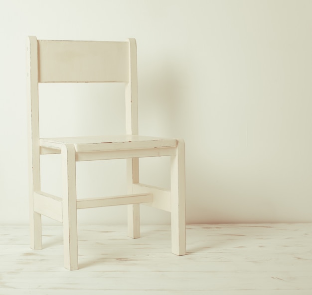 Single white rustic chair standing in an empty room on light wooden parquet floor.