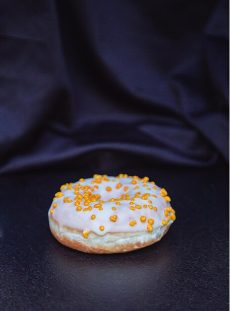 Photo single white sweet doughnut against black background junk fast food donut yellow sprinkles