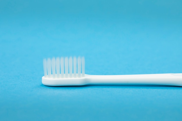 Single white toothbrush close up isolated on blue surface horizontal