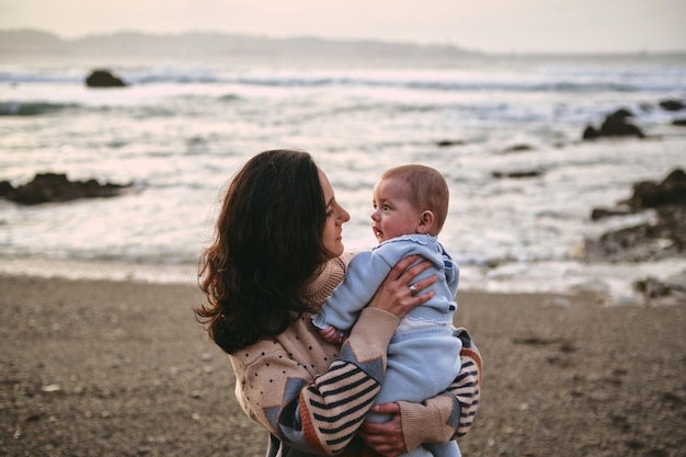 Одинокая молодая мать держит и смотрит на своего ребенка на пляже