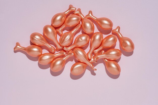 ピンクの背景に散らばった有効成分を持つ単一投与血清カプセル 皮膚ケアおよび美容製品