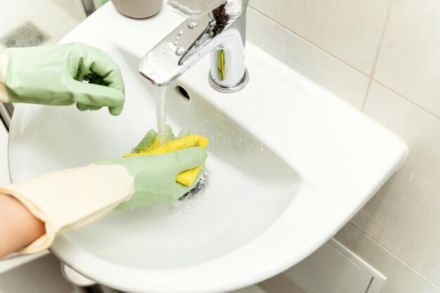 Photo sink cleaning female hands hold a yellow rag for cleaning the bathroom springcleaning