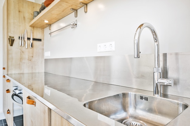 Sink with shiny tap installed under modern counter near jar with spices and gas stove in kitchen at home