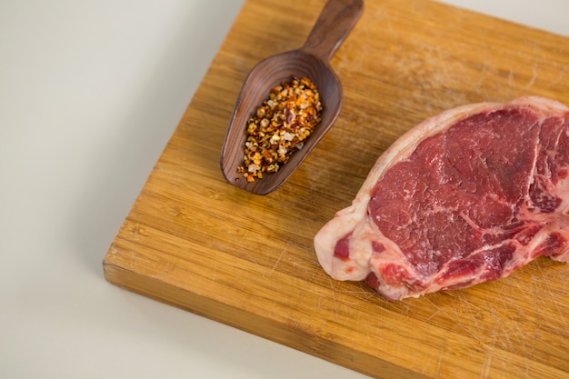 Sirloin chop and spices in wooden spoon on wooden board