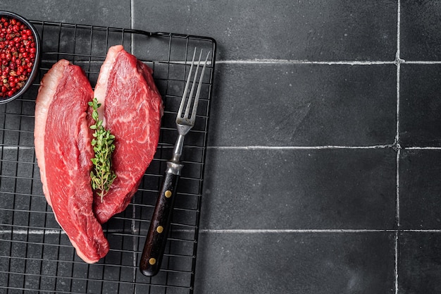 Sirloin steak or Cap Rump raw beef meat with herbs on a rack Black background Top view Copy space