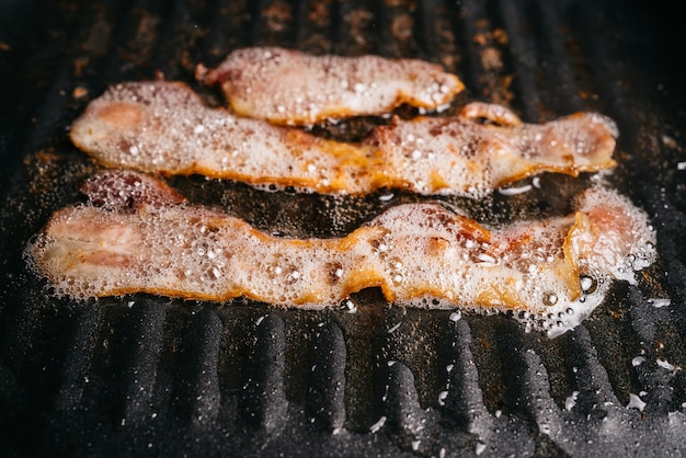 sissende spekreepjes bakken in een pan met hete smerende spekolie