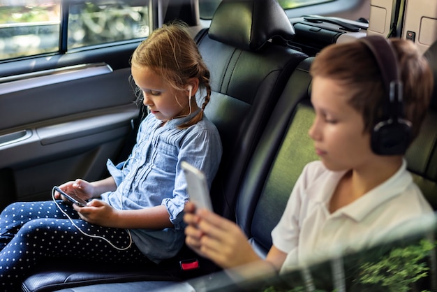 Sister and brother playing with digital devices in the car