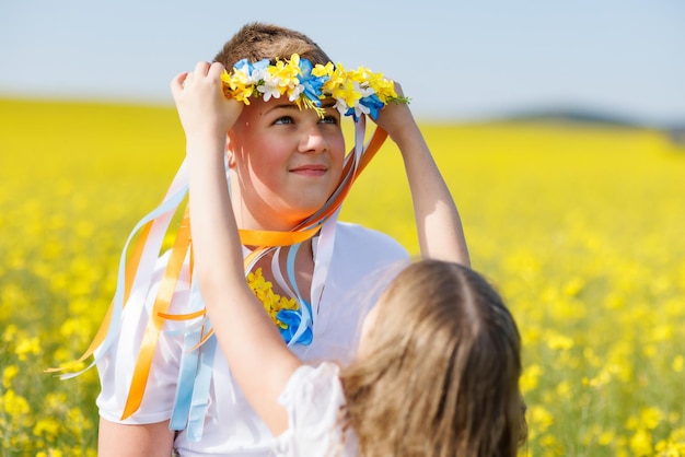 Sister puts on brother Ukrainian wreath with ribbons against background of fields and sky