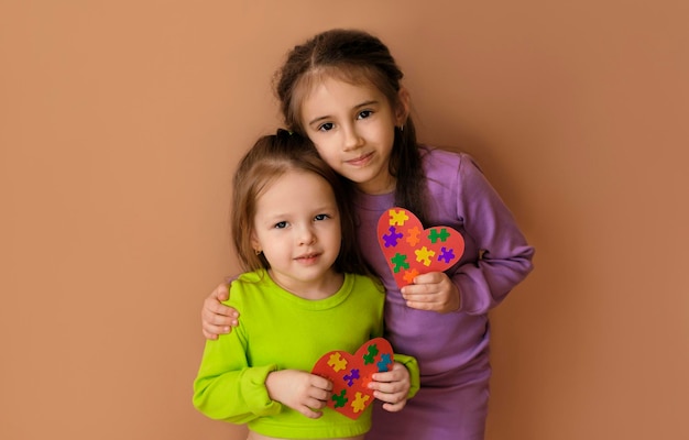 Sisters are holding puzzle hearts in their hands as a sign of support for kids suffering from autism