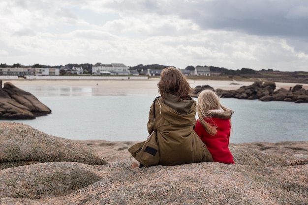 The sisters are sitting on the shore of the ocean  at  the Tregastel, Brittany. France