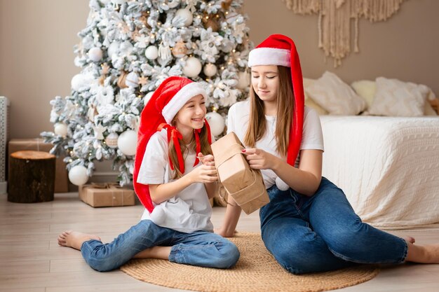 Sisters celebrate winter holidays girls exchange christmas gifts near christmas tree happy among new