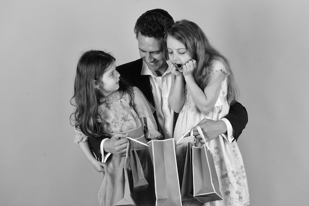 Sisters and father share presents Schoolgirls and dad hold pink packets looking inside Girls and man with surprised faces hold shopping bags on pink background Shopping surprise and family concept