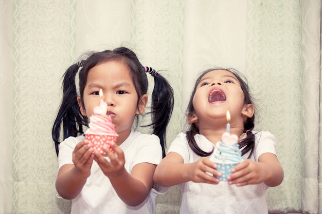 Sisters having fun blowing birthday cupcake together, Vintage color tone