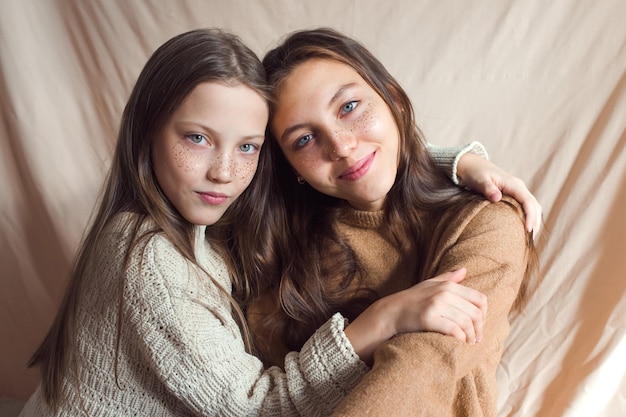 sisters hugging on beige color textile background