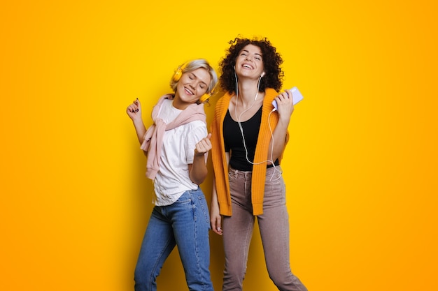 Sisters listening music on yellow wall for mobile device design online lifestyle lovely girls dancing