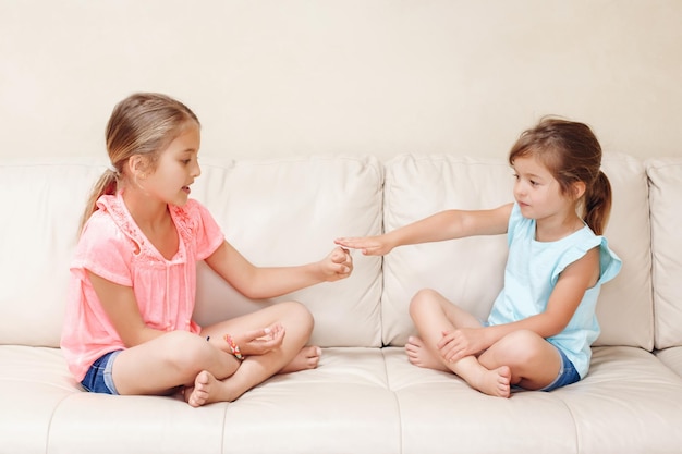 Photo sisters playing while sitting on sofa at home