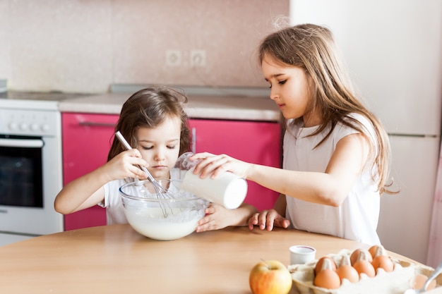 姉妹は朝食、ペストリー、ミックス小麦粉、牛乳、卵、ボウルにパンケーキを準備し、子供たちは母親、家族を助けます朝食、料理