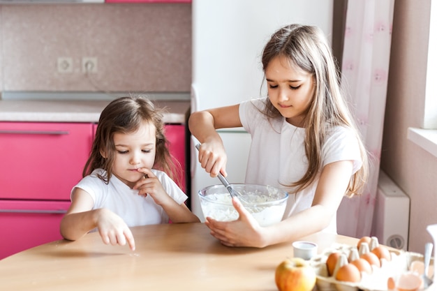 姉妹は朝食、ペストリー、ミックス小麦粉、牛乳、卵、ボウルにパンケーキを準備し、子供たちは母親、家族を助けます朝食、料理