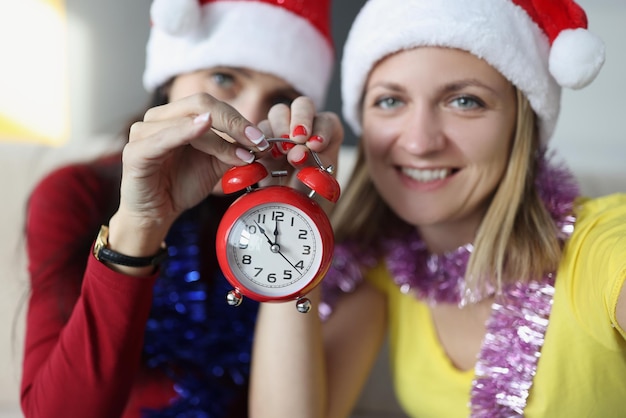 Sisters smile and hold red retro clock with arrows placed on midnight