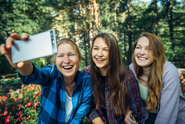 Photo sisters take a selfie on smartphone sitting in park on background of flowers on sunny day