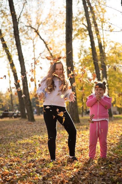Sisters throwing up dead leaves in autumn park