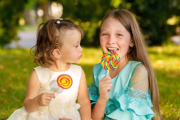 Sisters with sweet lollipops in nature in the summer in the park