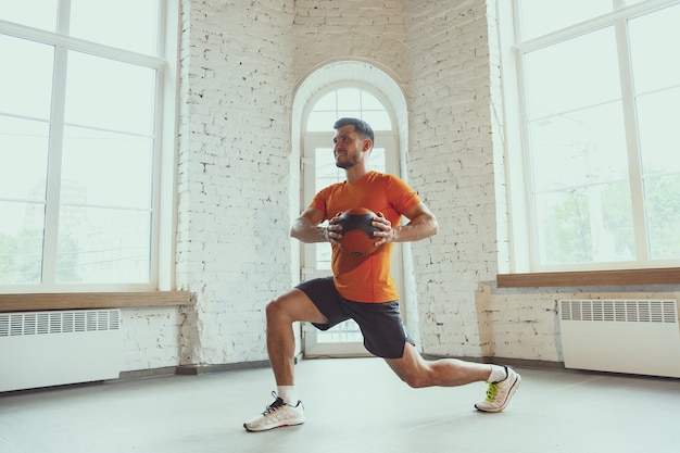 Sit ups with ball. Young caucasian man training at home during quarantine of coronavirus outbreak, doing exercises of fitness, aerobic. Sportive during insulation. Wellness, sport, movement concept.