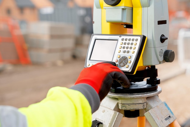 Site-ingenieur in hiviz die werkt aan een bouwplaats voor woningbouw met behulp van moderne landmeetkundige apparatuur