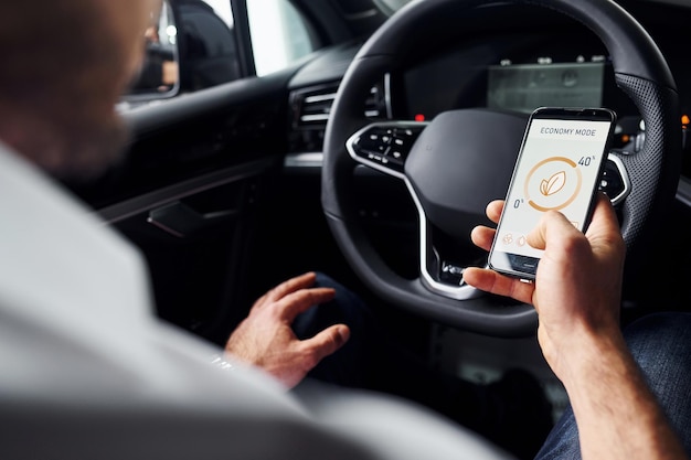 Sits in the car Close up view of man's hand that holds phone with labels and icons Conception of remote control