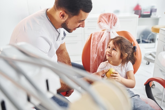 Photo sits on the chair little girl visiting dentist in clinic conception of stomatology