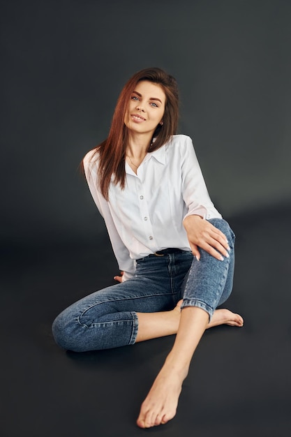 Sits on the floor Young beautiful woman is posing for the camera in the studio