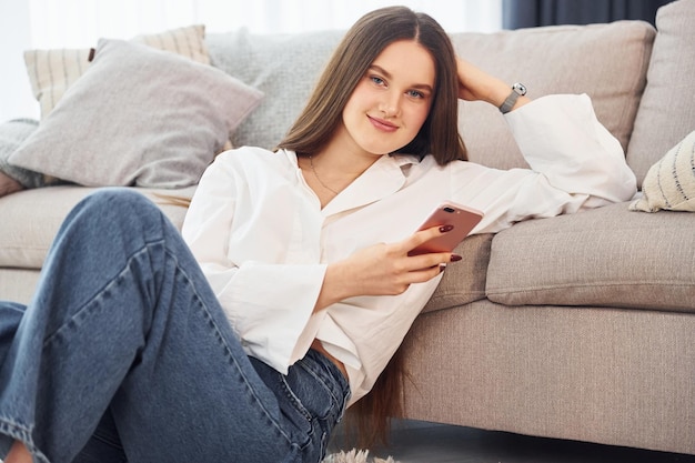 Sits on the floor Young woman in white shirt and jeans is at home