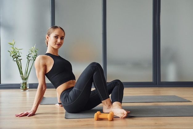 Si siede sul tappetino giovane donna in abbigliamento sportivo e con un corpo snello ha una giornata di yoga fitness al chiuso