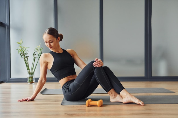 Si siede sul tappetino giovane donna in abbigliamento sportivo e con un corpo snello ha una giornata di yoga fitness al chiuso