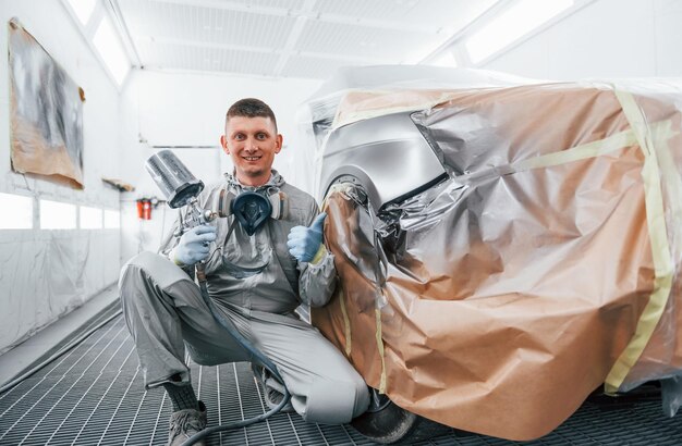 Sits near freshly painted car Caucasian automobile repairman in uniform works in garage