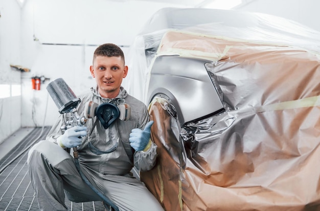 Foto si trova vicino a un'auto appena dipinta il riparatore di automobili caucasico in uniforme lavora in garage