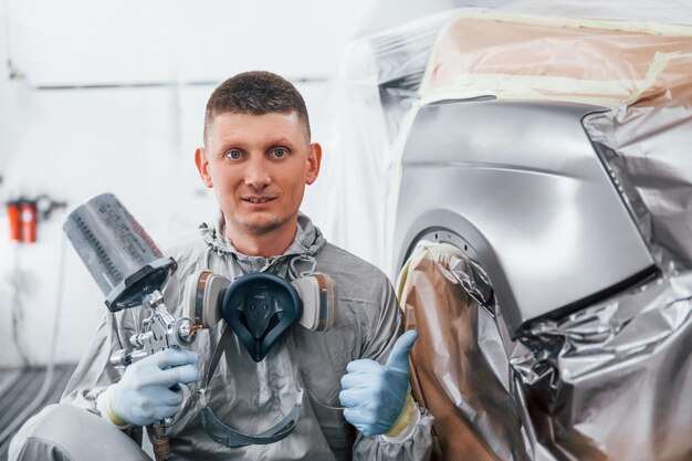 Sits near freshly painted car Caucasian automobile repairman in uniform works in garage