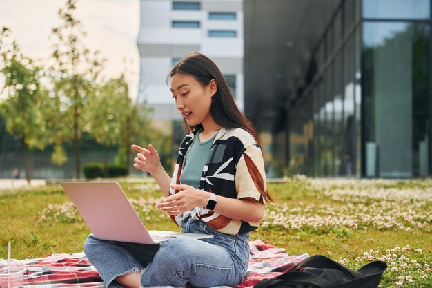 Sits with laptop Young asian woman is outdoors at daytime