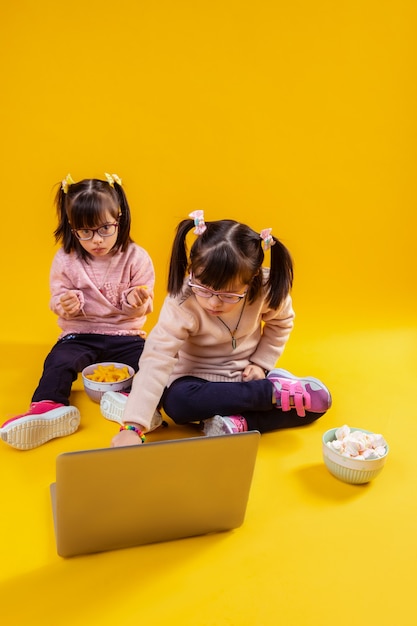 Sitting against laptop. curious small girls with genetic disorder spending time with laptop surrounded by bowls with snacks