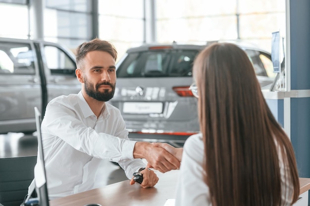 写真 座って握手をしている白い服を着た女性と男性が一緒に自動車ディーラーにいる