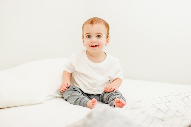 sitting baby in white tshirt on bed at home