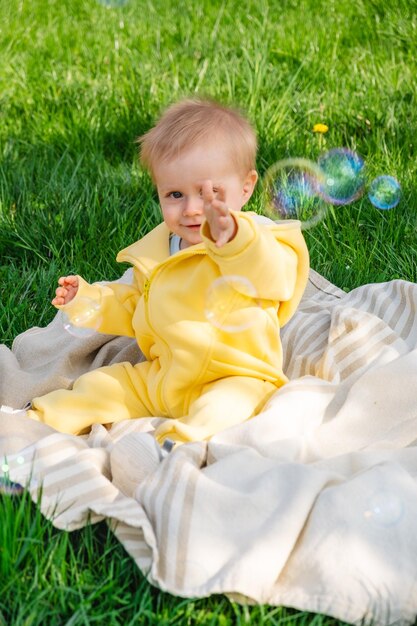 Sitting on a blanket a kid bursts bubbles in the park