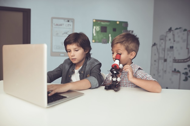 Sitting Boys Using Laptop and Microscope at Home.