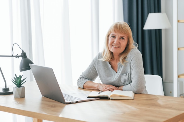 Sitting by table with laptop Senior woman with red hair is at home alone