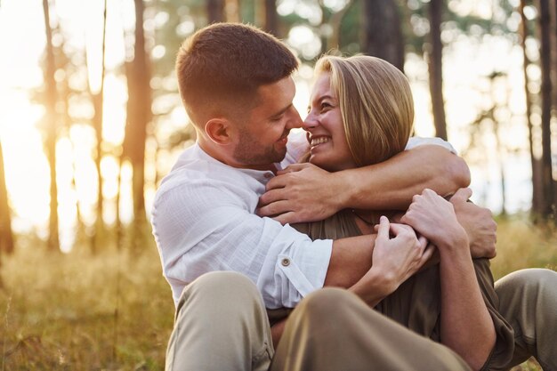 Sitting and embracing each other Happy couple is outdoors in the forest at daytime